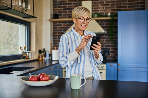istock A smiling senior woman using a mobile phone, standing in the kitchen, smiling. 1858536837