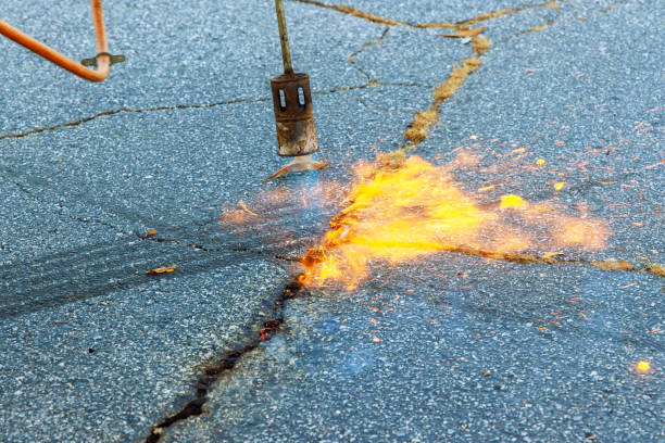 istock Worker performing road surface restoration on burning dry grass in asphalt cracks before coating with bitumen 1858545658