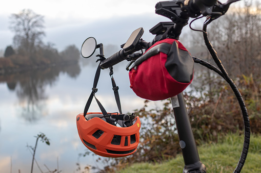 Orange bike helmet hangs from handlebar of an electric bike in the background a river on a winter day