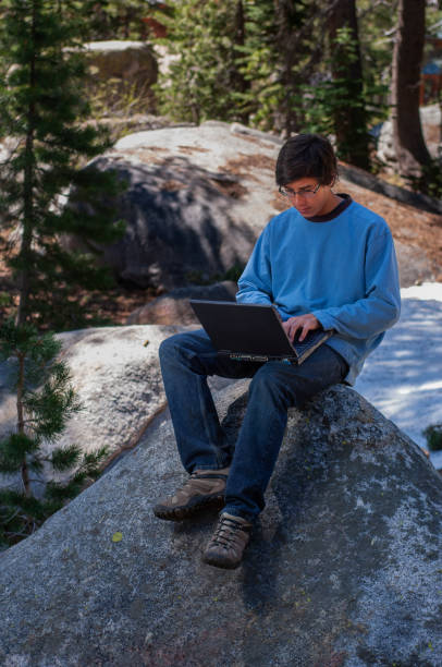 istock Teenager Sitting Atop a Large Boulder Working on Laptop Computer 1858594801