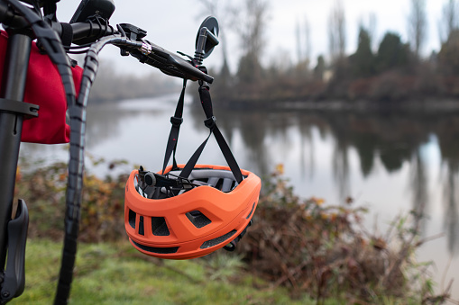 Orange bike helmet hangs from handlebar of an electric bike in the background a river on a winter day