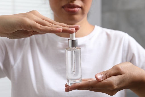 Woman with bottle of cosmetic serum on blurred background, closeup