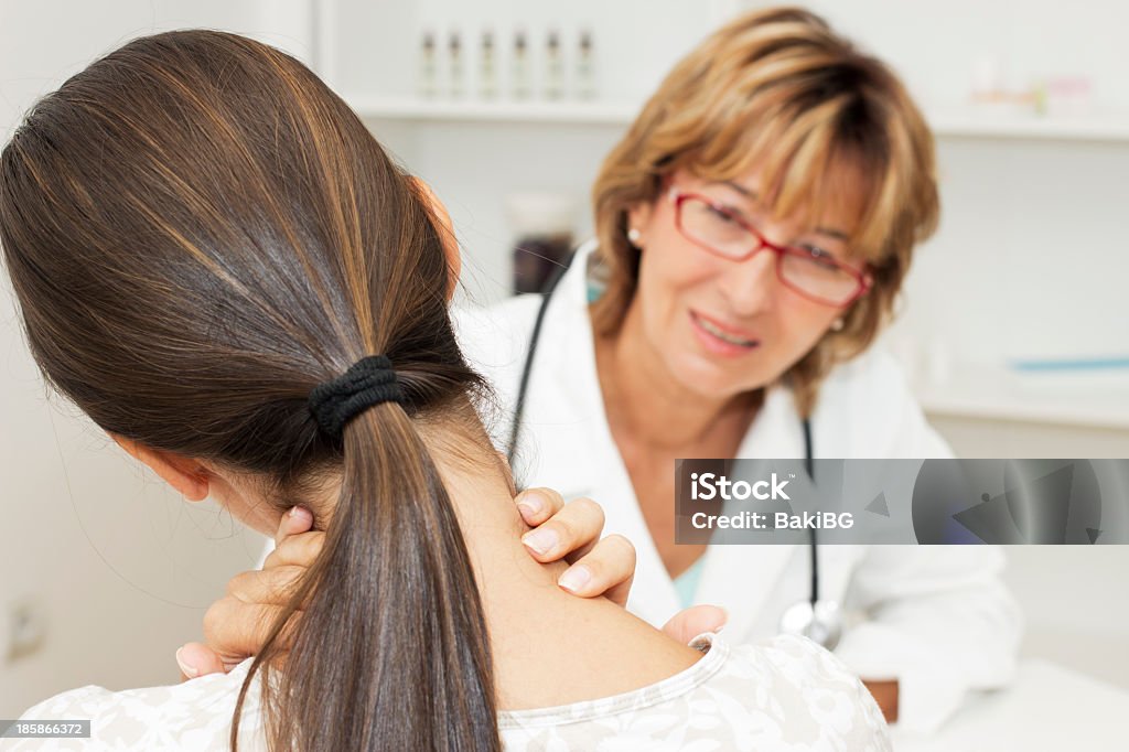 Back view of woman holding her neck and Doctor looking on Young woman holding her neck and talking with female doctor. Communication Stock Photo