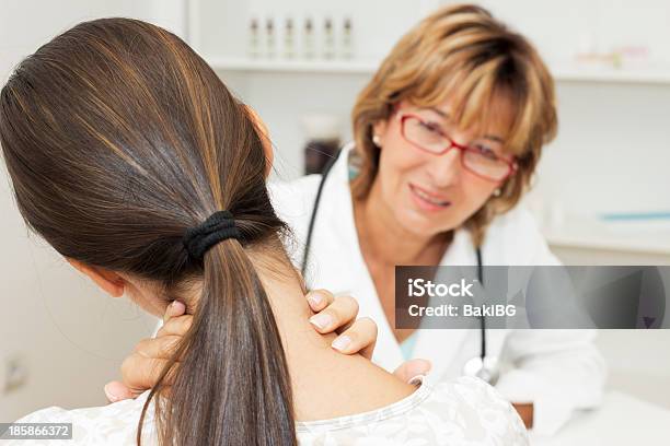 Back View Of Woman Holding Her Neck And Doctor Looking On Stock Photo - Download Image Now