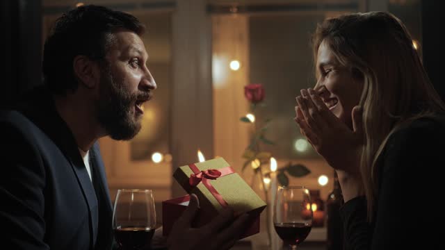 Gift, Valentines Day, wedding anniversary. Woman giving gift to man on date during romantic candlelight dinner