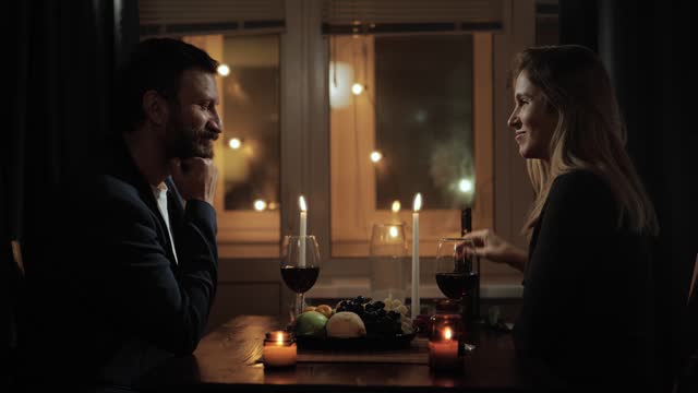 Date, Valentines Day, first date. Man gives one rose to woman during romantic candlelit dinner in restaurant or at home