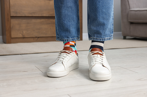 Man in different stylish socks, sneakers and jeans indoors, closeup