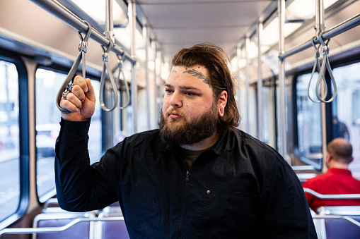 Images of the daily commute for a man going to work. He is dressed in black and is sporting cool face and hand tattoos. Image coveys professionalism and body art, as well as public transportation in an urban environment.