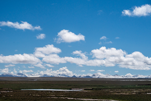 Plateau snow capped mountains and meadows under blue sky and white clouds