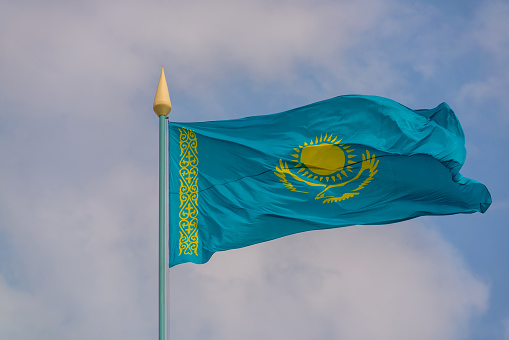 The state flag of the Republic of Kazakhstan fluttering in the wind with the image of the Sun and a flying eagle against the sky