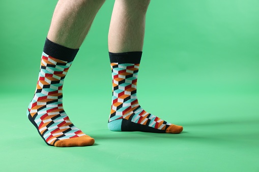 Man in stylish colorful socks on light green background, closeup. Space for text