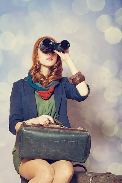 istock Redhead girl with binocular sitting on the big suitcase 185885581
