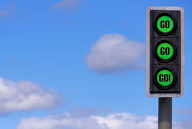 Business Motivational Concept: Go! x3 Traffic Lights Against a Blue Sky. All 3 are coloured Green with the words Go, Go, Go!  green light stoplight stock pictures, royalty-free photos & images