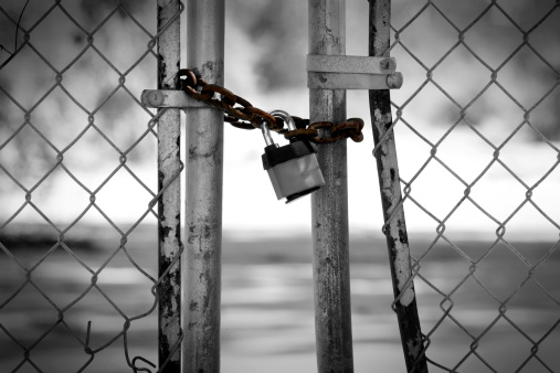 Old faded brown padlock and chain on an old weathered wooden gate.