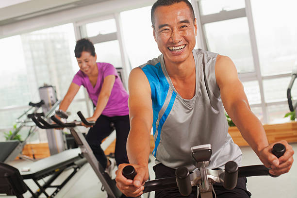 homme souriant, faire de l'exercice sur un vélo d'exercice - spinning instructor exercising gym photos et images de collection