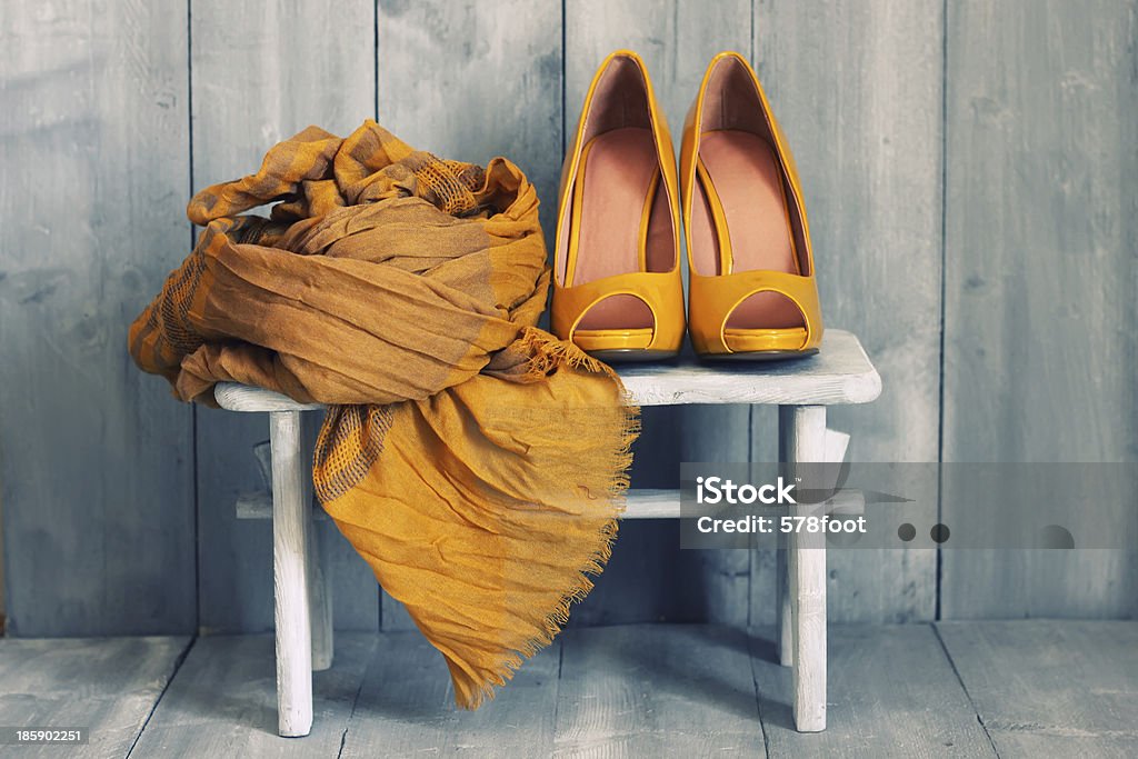 A white stool with dark yellow shoes and a scarf on it Photo of yellow shoes and scarf Scarf Stock Photo