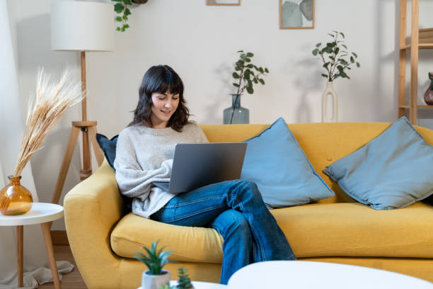 istock cheerful young woman using laptop while sitting on sofa at home 1859036222