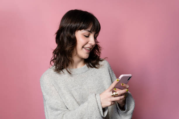 istock Cheerful young woman using her smart phone on a pink background 1859045159