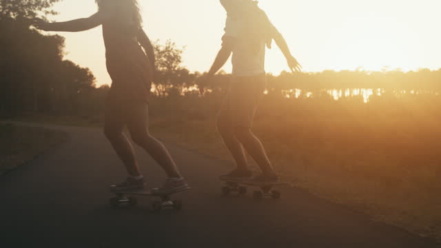 SLO MO Silhouette of couple having fun skateboarding on the road