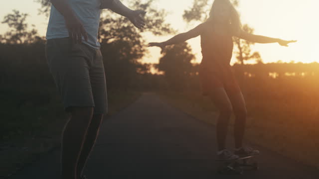 SLO MO Silhouette of couple having fun skateboarding on the road