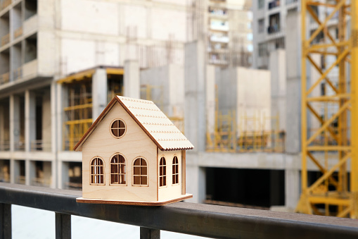 A beautiful wooden toy house against the backdrop of the construction of a new residential complex. Conceptual image. Selective focus.