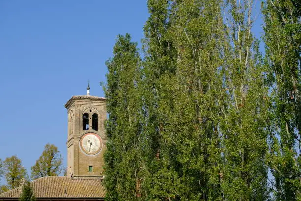 Church and bell tower of Roncole di Busseto (Parma). The church and the bell tower with a row of poplar trees. With the organ of this church the Italian composer Giuseppe Verdi learned to play. Before his death, Verdi had the church organ restored.  Stock photos. Busseto, Parma, Italy.