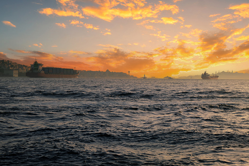 Two large transport ships with containers on deck float on the sea against the backdrop of the sunset sky.