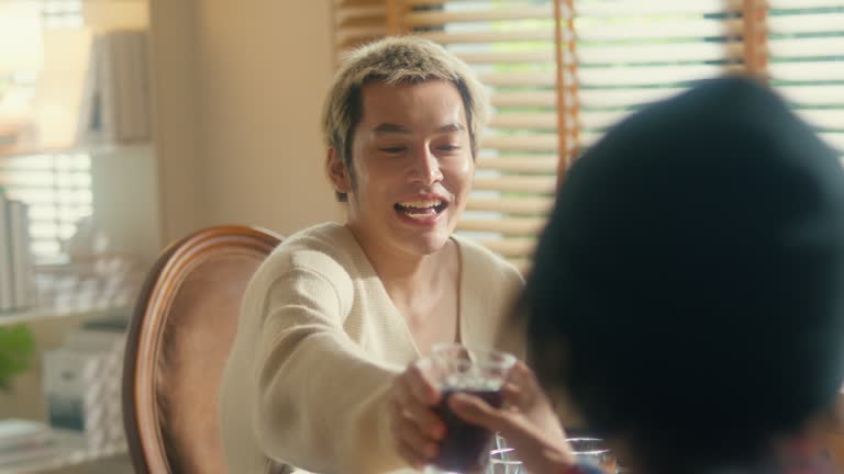 Group of young Asian people preparing and having fun sitting at dining table at home. Multicultural friends having fun together college house party.