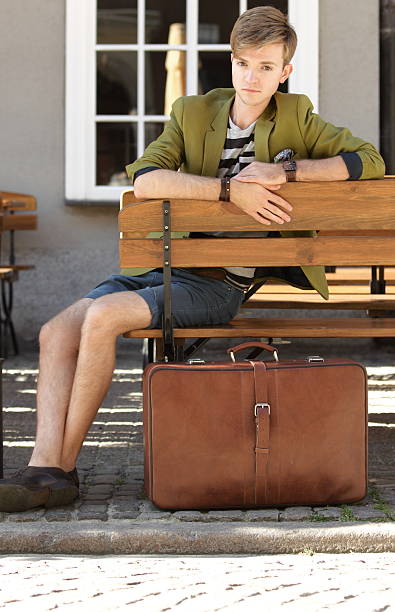 istock Young handsome man with suitcase waits on bench 185919742