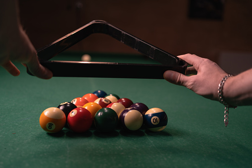 Male hands prepares sports game of billiards on a green cloth. Multi colored billiard balls in triangle with numbers. Copy space