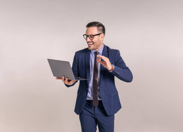 istock Cheerful male professional discussing over video call on laptop while standing over white background 1859234530