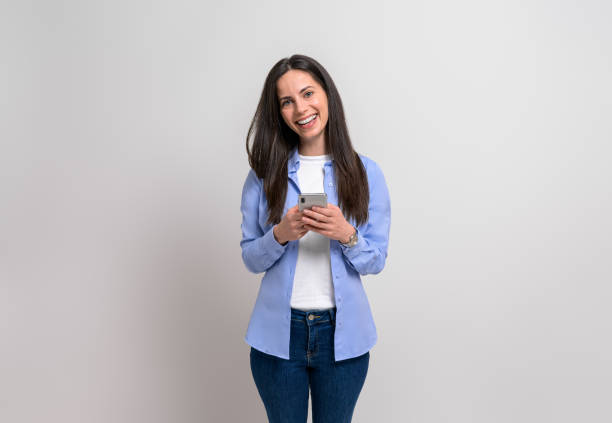 istock Smiling female professional texting over smart phone and looking at camera against white background 1859238676