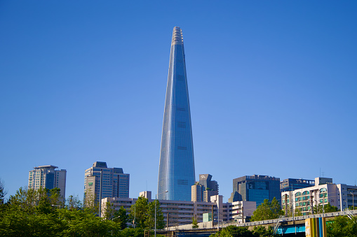 Seoul, South Korea - June 2, 2023: The Lotte World Tower towers above the small buildings of Songpa District, set against a clear blue sky with its tapered facade.