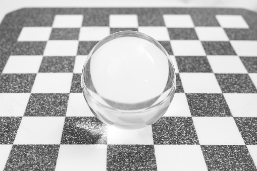 Glass lens ball on a marble chess board, soft focus
