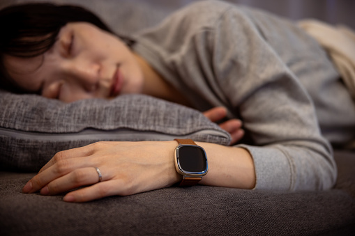 Woman sleeping at home, wearing smartwatch for sleep management - close-up