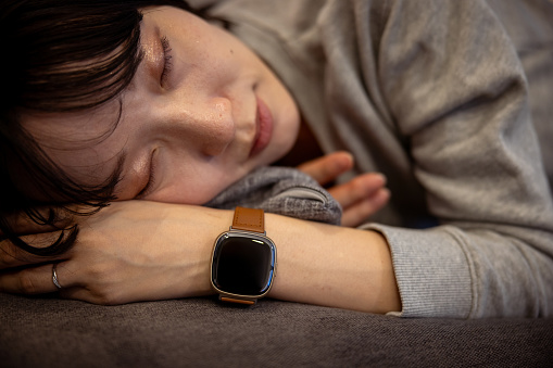 Woman sleeping at home, wearing smartwatch for sleep management - close-up
