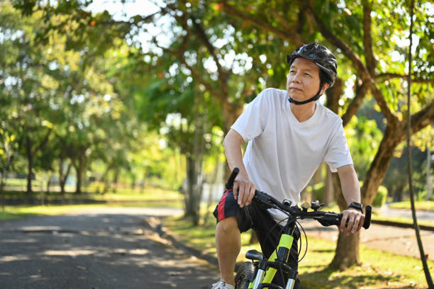 Active retired man in helmet riding bicycle in park on sunny summer day Active retired man in helmet riding bicycle in park on sunny summer day. man 60s bicycle stock pictures, royalty-free photos & images