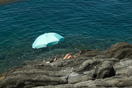 Riomaggiore, Cinque Terre. About 6/2020. Social distancing. Lonely woman in the Cinque Terre sea. Blue umbrella and blue sea.