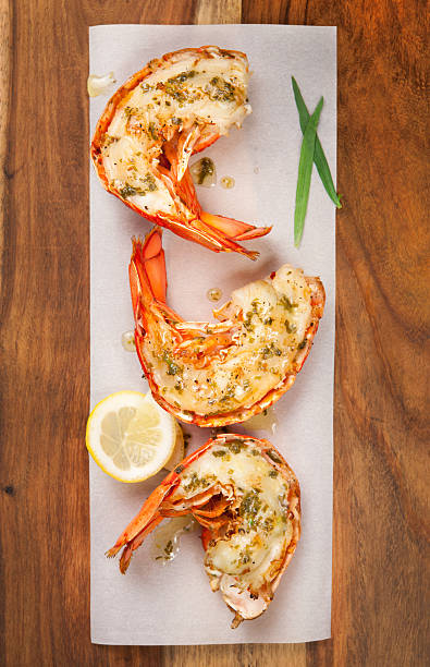Three grilled lobster tails on a plate Top view of grilled lobster tails with lemon tarragon butter tail fin photos stock pictures, royalty-free photos & images