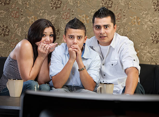 Scared Family Watching TV Scared young Latino family watching television together nail biting stock pictures, royalty-free photos & images