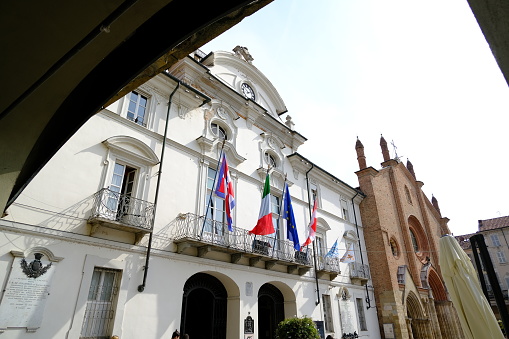 Asti, Italy. About 9-2021. Asti town hall.  Ancient Italian white palace with balcony and flags of Italy, Europe and Piedmont, waving in the wind.  Stock photos.