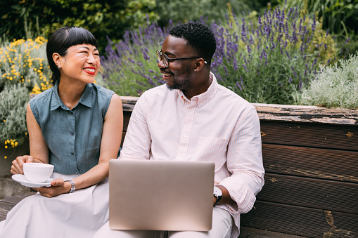 Transform the traditional office setting with the refreshing vibes of a park bench, where an African-American man and an Asian woman work together on a laptop, radiating positivity and cooperation.