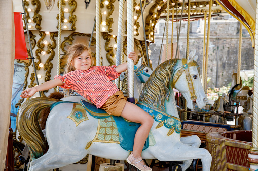 Happy positive preschool girl having a ride on the old vintage merry-go-round in city of St Malo France. Smiling child on a horse