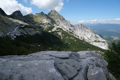 Mountains of the Apuan Alps between Monte Pisanino and Monte Cavallo. The fronds of the green trees contrast with the blue of the sky and the clouds. On the side of the Garfagnana delle Apuane there are numerous white marble quarries. The excavation is producing an environmental disaster as the mountains are destroyed to extract the marble. Foto stock royalty free. Alpi Apuane, Garfagnana, Italy.