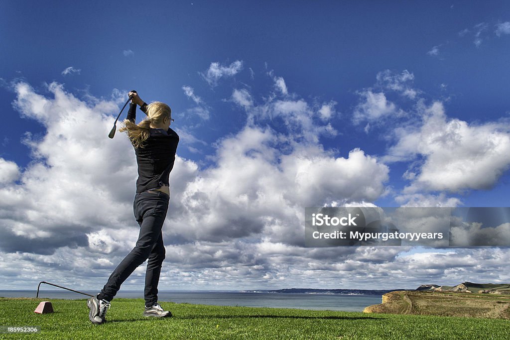 At the tee A woman watches her ball fly down the fairway having struck it from the tee with a stunning backdrop of sky and sea Driver - Golf Club Stock Photo