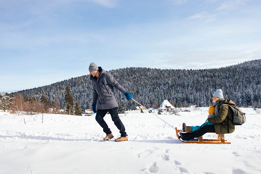 A side view of a smiling Caucasian family having fun on the snow using sledge.