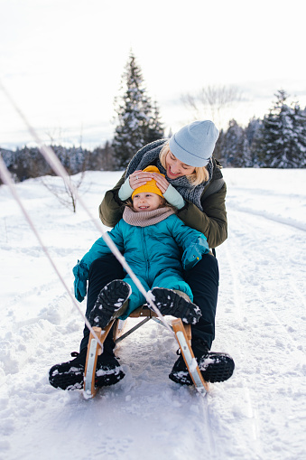 A smiling Caucasian baby girl looking away while having fun with her mother on  the snow.