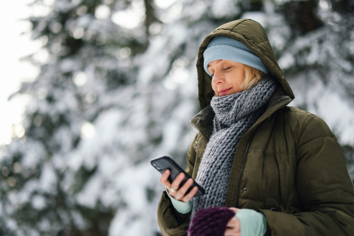 A smiling Caucasian female texting on her mobile phone while relaxing on a cold winter day.