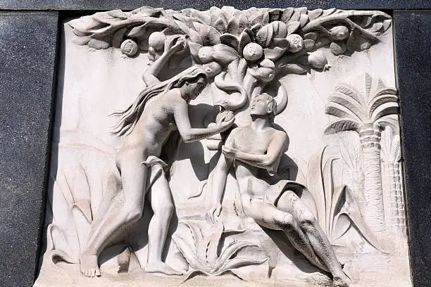 Milan, Italy. Old biblical scene sculpture at the Monumental Cemetery (Cimitero Monumentale). Religious art depicting Adam and Eve picking the fruit in the garden of Eden.