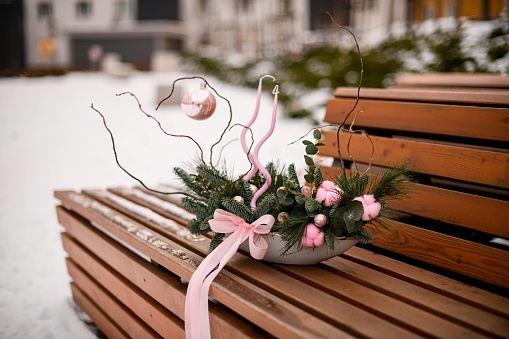 Christmas bouquet of fir branches with a pink tree toys and a pink ribbon on a bench on the city street